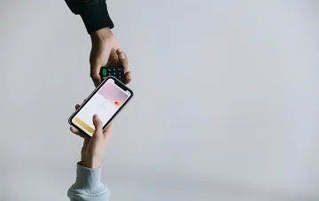 Übergabe eines Smartphones mit offenem Apple Wallet für kontaktlose Zahlung auf dem iPhone