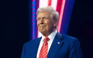 Donald Trump im blauen Anzug mit US-Flagge am Revers auf der Bühne nach der Erklärung zur Entminung der Straße von Hormus und den Drohungen gegen den Iran
