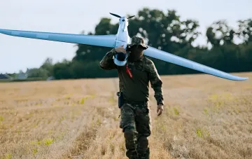 Военнослужащий несёт на плече украинский разведывательный дрон на фоне поля — иллюстрация мощностей оборонной промышленности Украины