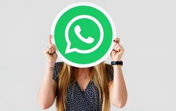 Женщина держит перед лицом логотип WhatsApp на фоне новости о отказе Meta от шестизначного PIN-кода в пользу длинных паролей и паскеев