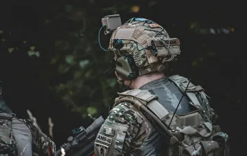 Військовий у камуфляжі з високотехнологічним шоломом, оснащеним датчиками та камерою, на тлі лісу — ілюстрація до теми впливу ШІ на збір даних на полі бою