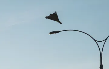 A jet-powered drone flies over Kyiv against a clear sky near a street lamp during the August 27 drone attack