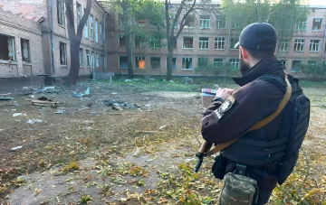 Полицейский осматривает последствия ночной атаки на Киев: разрушенные окна и обломки в дворе жилого дома