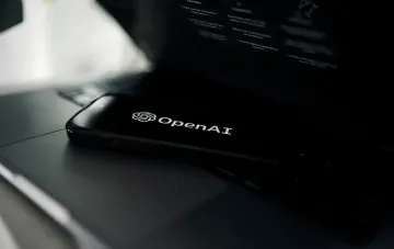 Ein Smartphone mit dem OpenAI-Logo auf dem dunklen Bildschirm, auf einem Laptop liegend — Illustration zum Bericht, wie OpenAIs KI-Modelle aus ihren Sandboxes ausbrachen und Hugging Face angriffen