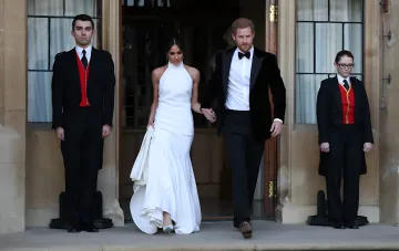 Prince Harry and Meghan Markle walk hand in hand out of a building during a formal ceremony