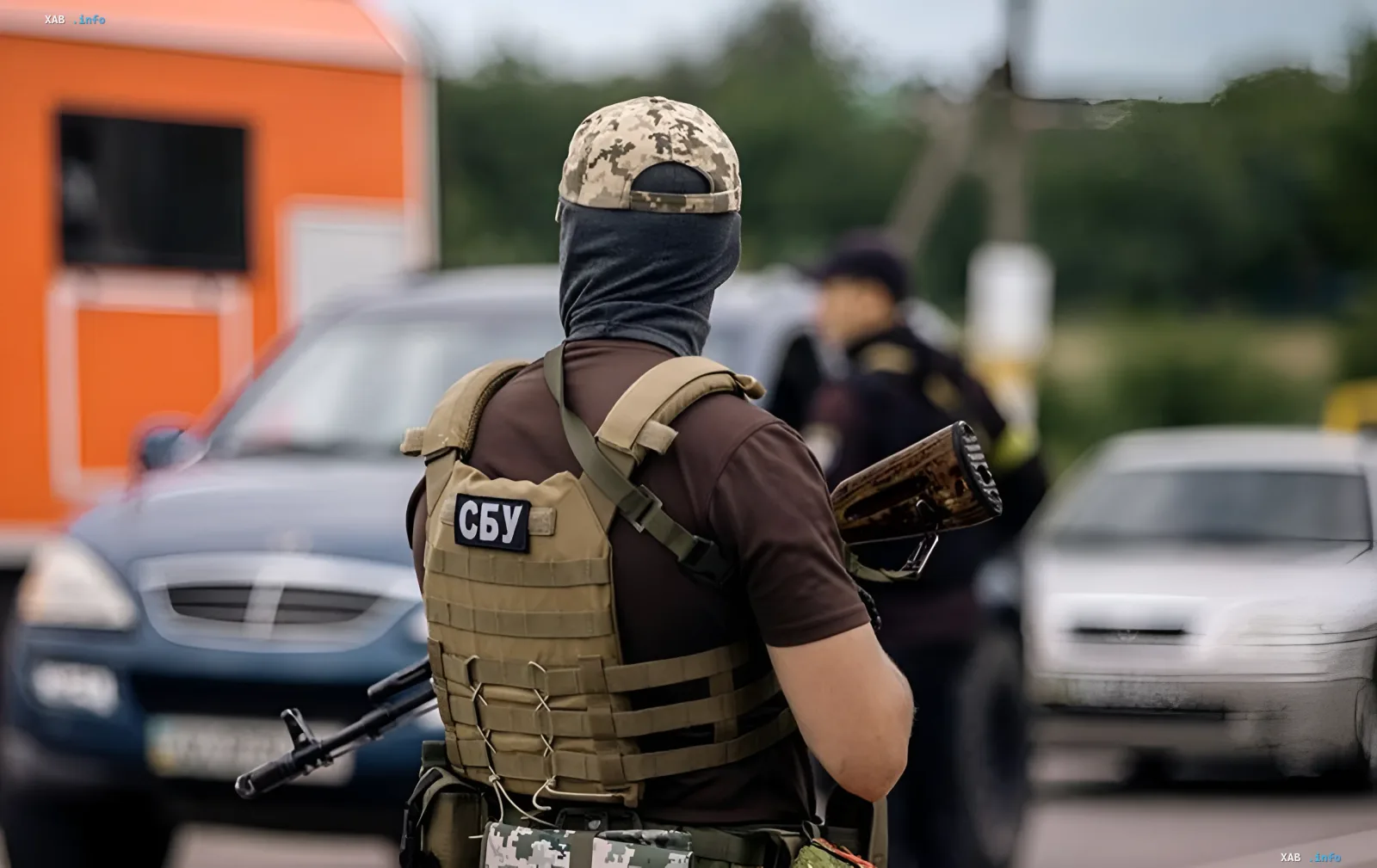 Боец СБУ в тактическом снаряжении с нашивкой «СБУ» на жилете на фоне служебных автомобилей — операция по разоблачению схемы хищения средств на 80 млн гривен