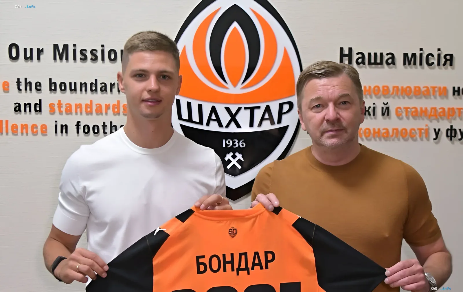 Valeriy Bondar and a Shakhtar representative holding the club jersey in front of the Shakhtar logo