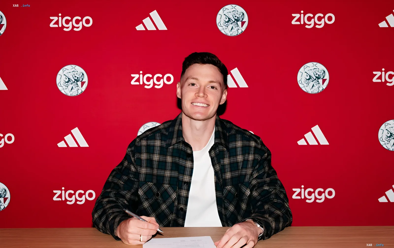 Vladimir Tsygankov signs his contract with Ajax against the club's logo backdrop