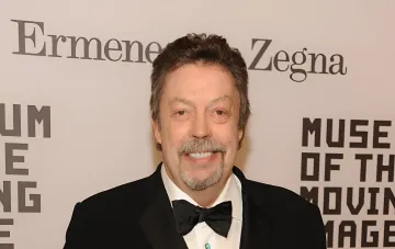 Тим Карри в чёрном смокинге с бабочкой на фоне логотипов Ermenegildo Zegna и Museum of the Moving Image
