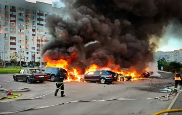 Burning cars and thick smoke after a nighttime drone and glide bomb attack, firefighters work to extinguish the fire near residential buildings