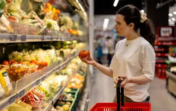 Käuferin wählt Tomaten an einer Supermarktregalreihe aus, umgeben von Gemüsen des Borsch-Sets vor dem Winterpreisanstieg