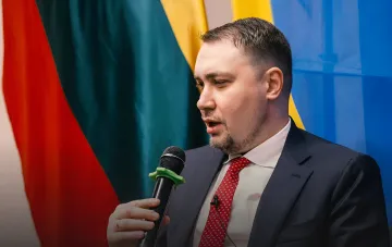 Кирилл Буданов выступает с микрофоном на фоне государственных флагов, комментируя протесты в Украине 2025 года