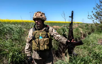Український військовий з автоматом у полі на тлі рапсових полів — питання зарплати після СЗЧ