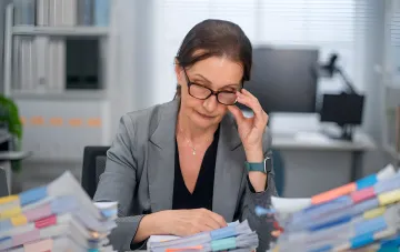 Geschäftsfrau prüft Stapel von Dokumenten mit farbigen Lesezeichen im Büro während der Vorbereitung auf eine Steuerprüfung