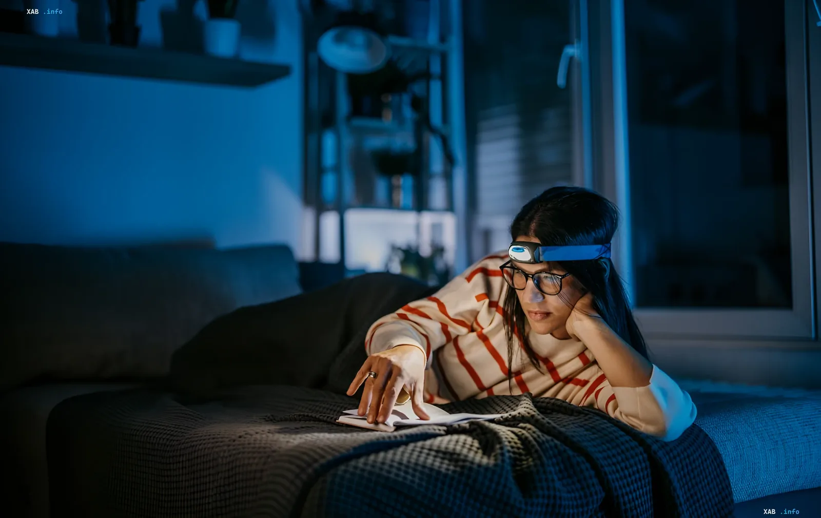 Woman reading a book in the dark with a headlamp, illustrating practical blackout preparation