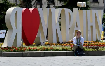 Человек отдыхает у инсталляции «Я люблю Украину» на фоне цветущей клумбы в тёплый летний день в Украине