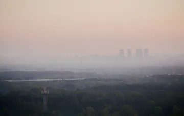 Vergilfter, smogverhangener Horizont über Wald und Hochhäusern in der Oblast Kiew nach russischen Angriffen, verschlechterte Luftqualität