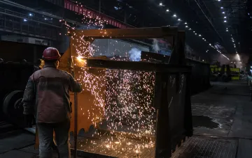 Arbeiter in einem ukrainischen Stahlwerk beim Schweißen von Metall vor funkenübersättem Hintergrund — die Branche steht in einer systemischen Krise