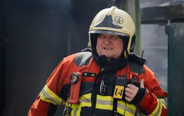 Firefighter in full gear with radio and flashlight amidst smoke after attack on Epicenter construction store in Zaporizhzhia