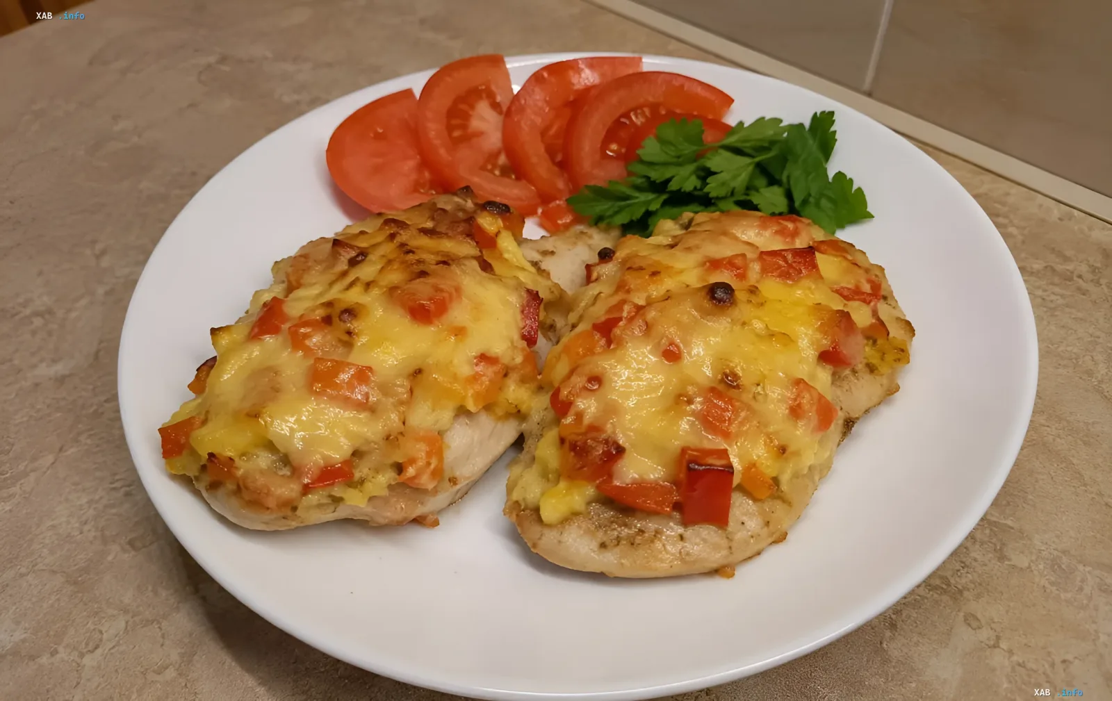 Куриное филе под творожно-овощной шапкой с красным перцем, запечённое в духовке, поданное на белой тарелке со свежими помидорами и петрушкой