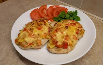 Куриное филе под творожно-овощной шапкой с красным перцем, запечённое в духовке, поданное на белой тарелке со свежими помидорами и петрушкой