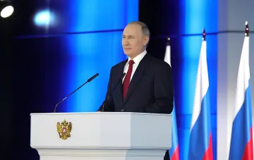 Владимир Путин за трибуной с гербом России на фоне флагов РФ; приезд президента в Нижний Новгород совпал с топливным кризисом и очередями за бензином