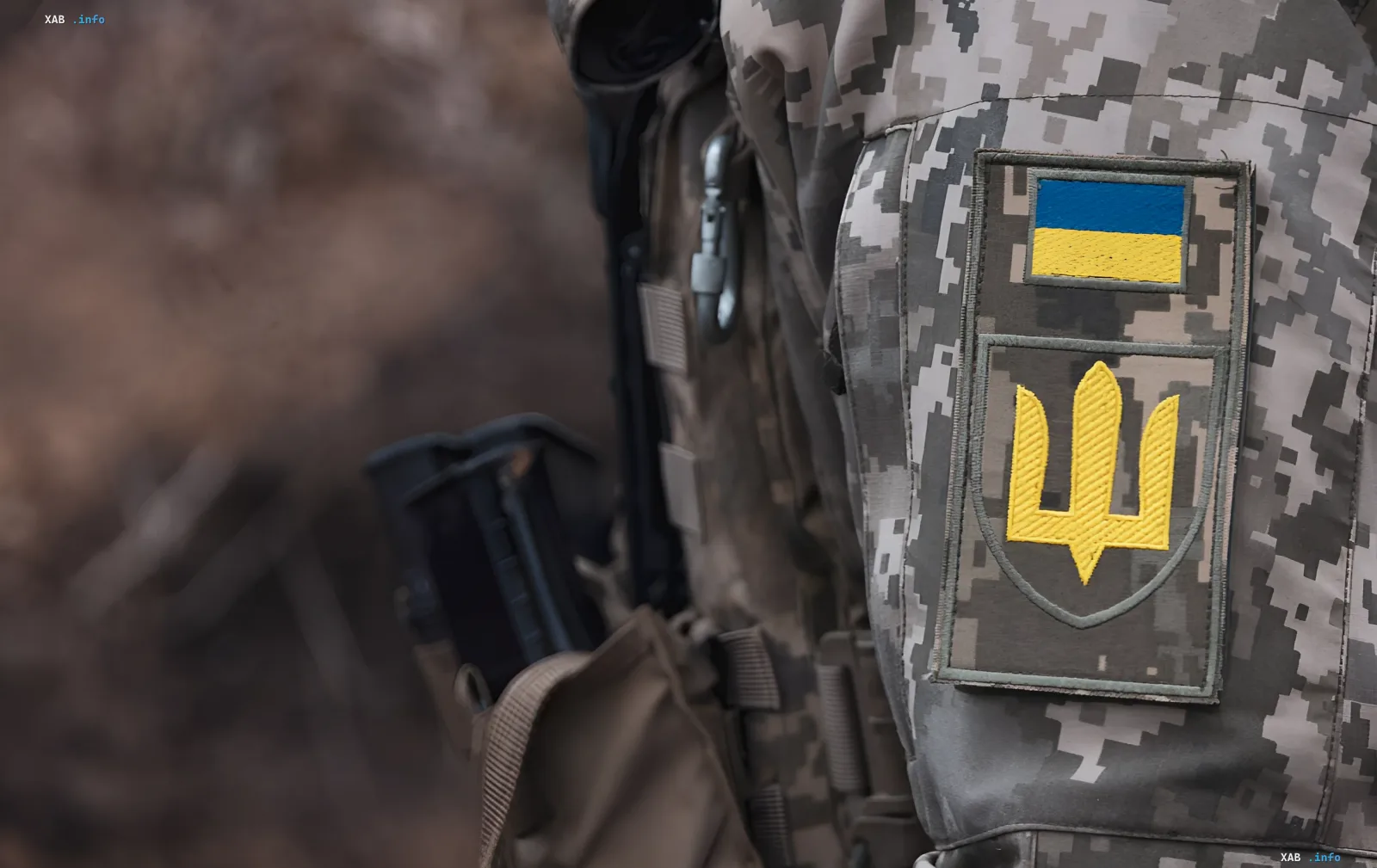 Украинский солдат в камуфляжной форме с нашивками флага и тризуба на фоне сообщений ОП о снижении темпов продвижения российских войск на фронте