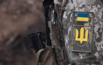 Украинский солдат в камуфляжной форме с нашивками флага и тризуба на фоне сообщений ОП о снижении темпов продвижения российских войск на фронте