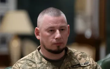 Украинский военный в камуфляжной форме с нашивкой ВСУ на фоне интервью о проблемах ПВО с реактивными дронами РФ