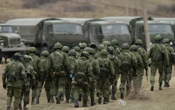 Российские военные в камуфляже и шлемах уходят от колонны грузовиков на фоне статистики потерь армии в Украине