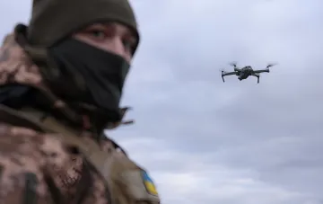 Военнослужащий ВСУ наблюдает за летящим боевым квадрокоптером на фоне облачного неба в зоне боевых действий