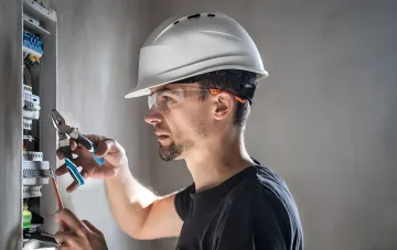 Elektriker mit Schutzhelm und Schutzbrille arbeitet an einem Verteilerkasten — Beispiel eines Produktionsberufs, dessen Gehalt in der Ukraine auf 50.000 Hrywnja stieg