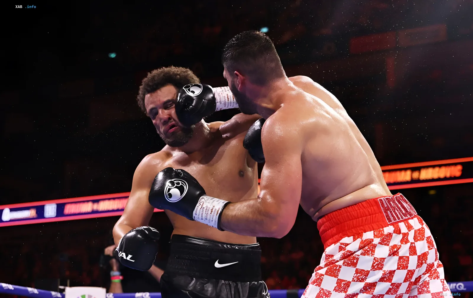 Boxing match in the ring: a fighter in red and white checkered shorts lands a powerful punch on an opponent in black shorts
