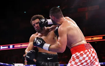 Boxing match in the ring: a fighter in red and white checkered shorts lands a powerful punch on an opponent in black shorts