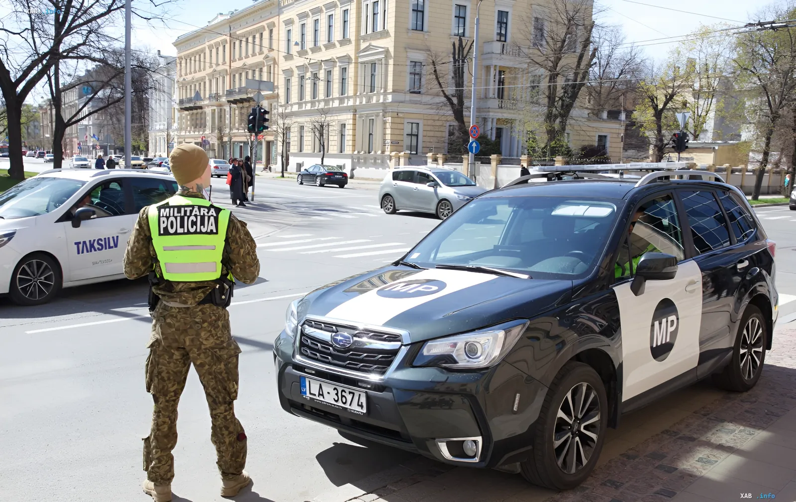 Солдат литовской военной полиции в камуфляже и сигнальном жилете у служебного автомобиля MP на фоне исторического центра Вильнюса — усиление мер безопасности в связи с провокациями у оборонных компаний