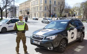 A Lithuanian military police soldier in camouflage and a high-visibility vest beside an MP service vehicle in the historic centre of Vilnius — heightened security amid provocations at defence companies