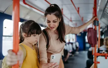 Mother and schoolgirl in the metro looking at a smartphone, preparing to apply for a digital student pass