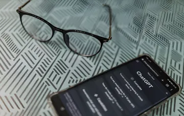 A smartphone displaying the ChatGPT interface on a background of glasses and newspaper, illustrating OpenAI's update to private chats
