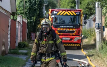 Пожарный в защитном снаряжении на фоне пожарного автомобиля после ночных ударов по Киевской области