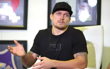 Александр Усик в чёрной футболке USYK жестикулирует во время интервью, комментируя сенсационную победу Хрговича над Итаумой