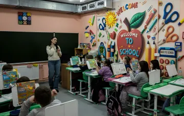 Учительница проводит урок в начальной школе на фоне декорации Welcome to School — иллюстрация к новости о повышении зарплат педагогов в Украине на 20% с 1 сентября