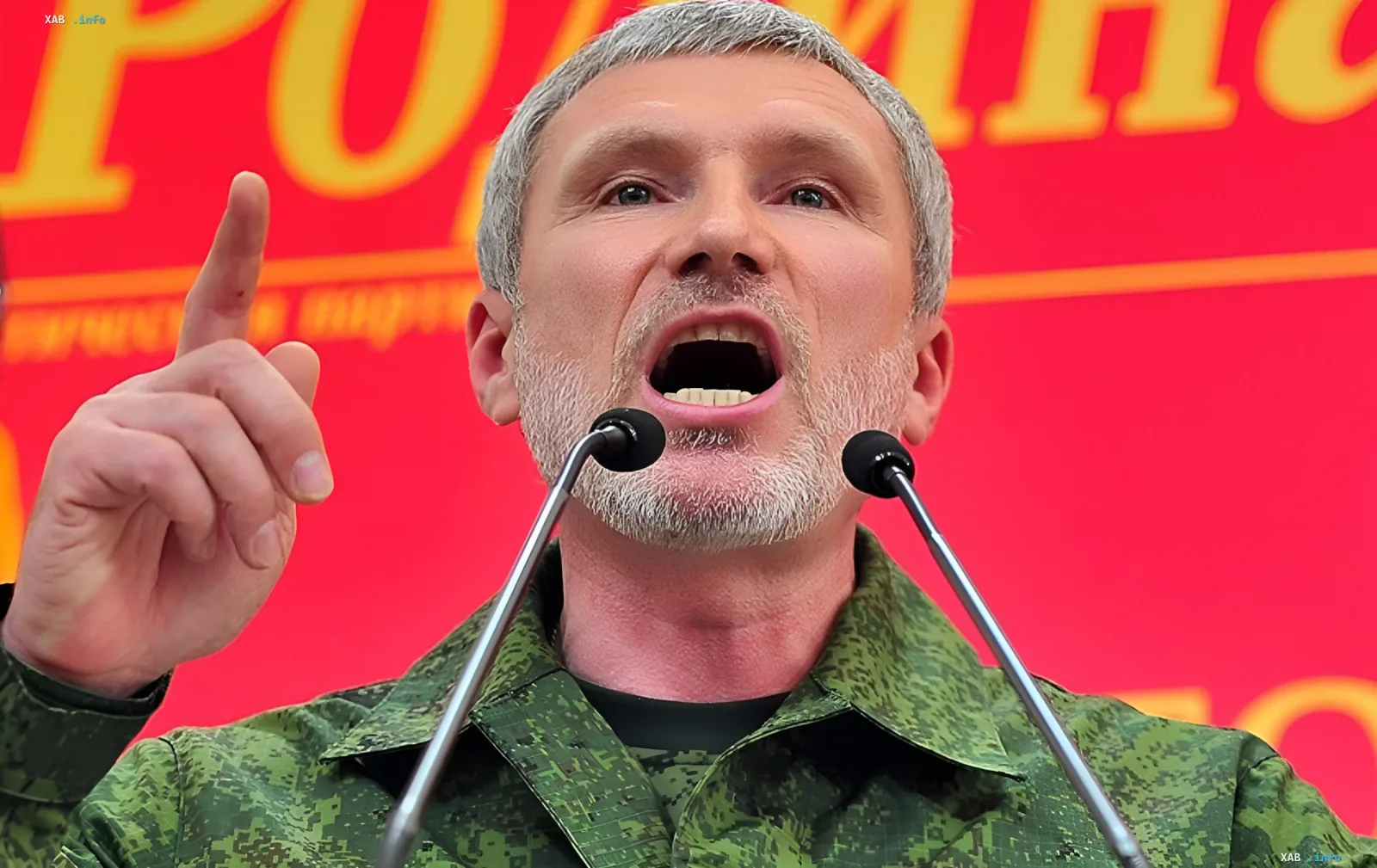 Мужчина в камуфляжной форме на публичном выступлении у микрофонов, жестикулирующий на фоне красного баннера — иллюстрация к заявлению о применении тактического ядерного оружия