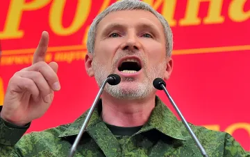 Мужчина в камуфляжной форме на публичном выступлении у микрофонов, жестикулирующий на фоне красного баннера — иллюстрация к заявлению о применении тактического ядерного оружия