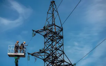 DTek energy workers on a lift repairing a high-voltage transmission tower to restore electricity