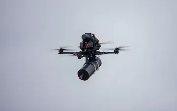 Militärer Quadrocopter-Drohne mit aufhängtem Modul im Flug — Illustration zum Glasfaserdrohnen-Ausschreibungsverfahren und zur NABU-Beschwerde