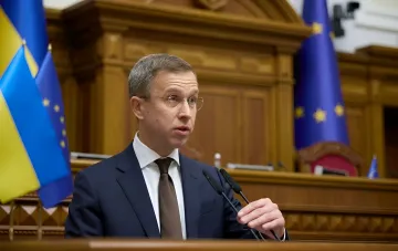 Speech at a podium against Ukrainian and EU flags in the context of strict budget austerity and closing the state budget deficit