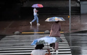 Fußgänger mit Regenschirmen überqueren eine nasse Straße in Kiew während eines Gewitters — gelbes Warnlevel am 1. September
