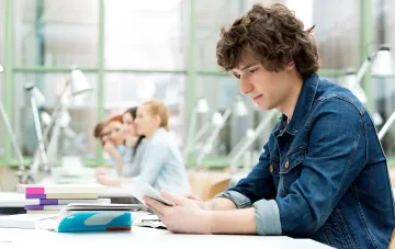 Student with a tablet and textbooks at a desk in a Ukrainian university classroom at the start of the new academic year