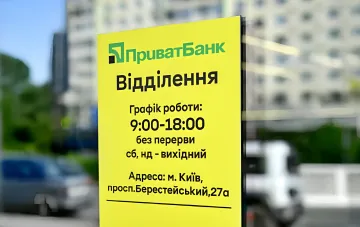 Yellow PrivatBank information sign in Kyiv showing branch working hours, temporarily adjusted during air raid alerts