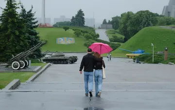 Пара под розовым зонтом идёт по мокрой площади Военного городка в Киеве в дождливую погоду при прогнозе холодного фронта 2 сентября